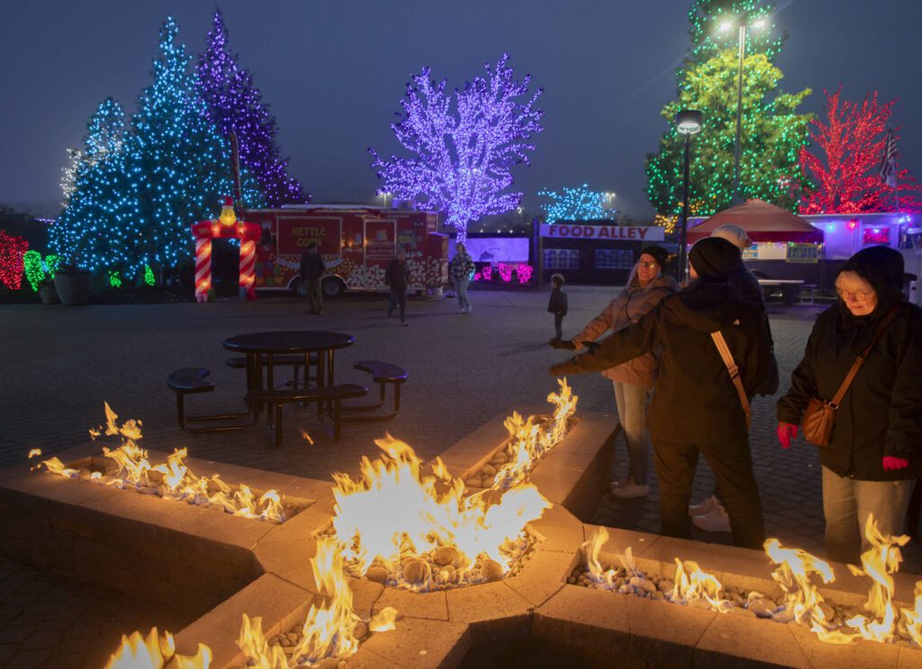 People gather around the fire pit to warm themselves up in the center of the vendor village at Tulalip Lights & Ice on Wednesday, Dec. 4, 2024 in Tulalip, Washington. (Olivia Vanni / The Herald)
